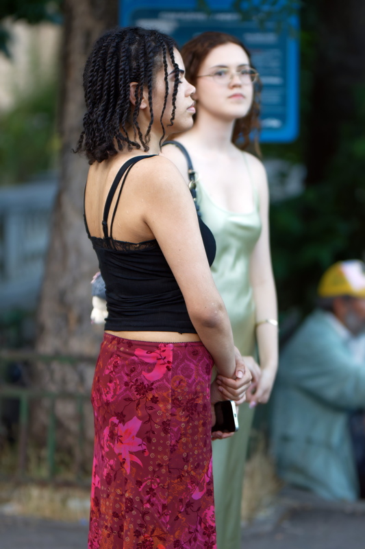 coming_soon_8 - Two individuals standing outdoors, with one wearing a black tank top and a red patterned midi skirt